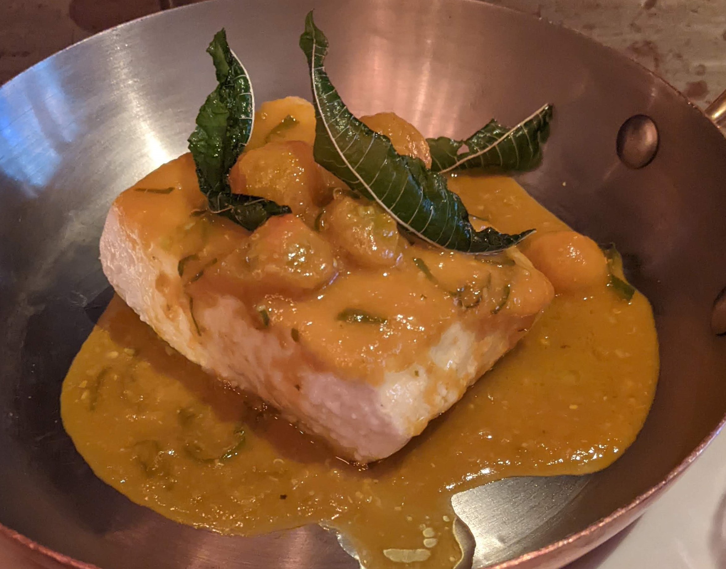 A filet of halibut in a silver dish, covered in yellow tomato sauce